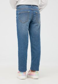 Jasnoniebieskie dżinsy o prostym kroju, z dwiema tylnymi kieszeniami i wygodnym elastycznym pasem, w połączeniu z kolorowymi, refleksyjnymi sneakersami.