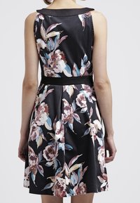 Šaty s květinovým potiskem, černým pozadím, jemnou tkaninou, bezrukávovým designem a páskem v pase s sklady na zadní straně.