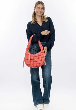 Gepolsterte Koralltasche mit einem gesteppten Design, ausgestattet mit einem weichen, breiten Schulterriemen und zwei Kordelzugakzenten, kombiniert mit ausgestellten Jeans und Sneakers.