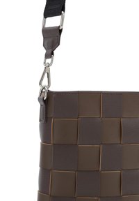 Hnědá tkaná kožená kabelka s texturovaným povrchem, která má odnímatelný černý popruh a stříbrné kovové detaily pro připevnění.