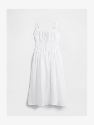 White midi dress with thin straps, gathered waist, ruched bodice, and a loose, textured skirt.