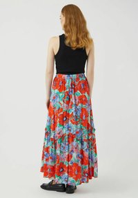 Falda maxi con un patrón floral en rojo, azul y verde, con un diseño escalonado y cintura elástica, combinada con una camiseta sin mangas negra y zapatos.
