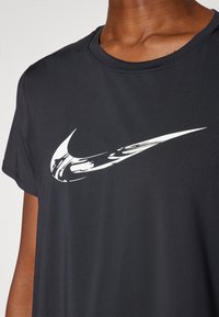 Svart Nike t-skjorte med en fremtredende hvit swoosh-logo. Stoffet virker glatt med en klassisk rund halsdesign og korte ermer.