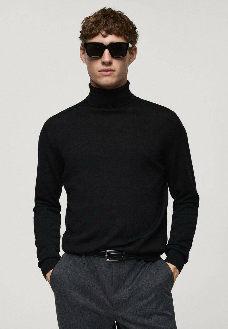 Schwarzer Rollkragenpullover aus Strickstoff, taillierte Passform, gerippte Bündchen. Getragen mit grauen Hosen und schwarzen Sonnenbrillen.