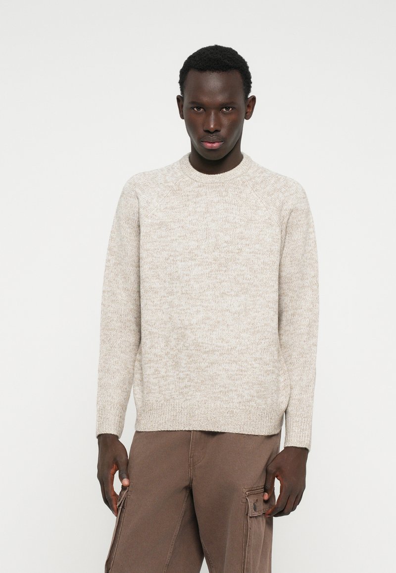 Light beige knitted sweater with a round neck and long sleeves, featuring a textured fabric and ribbed cuffs, paired with brown cargo pants.