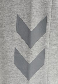 Deux formes de chevrons gris foncé orientées vers le bas imprimées sur un tissu gris clair texturé, probablement partie d’un vêtement.