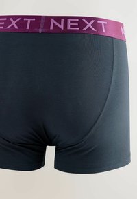 Férfi sötétkék boxeralsó, burgundi színű, kontrasztos elasztikus derékrésszel, amelyen a "NEXT" felirat világoslila színben szerepel. Simább tapintás.