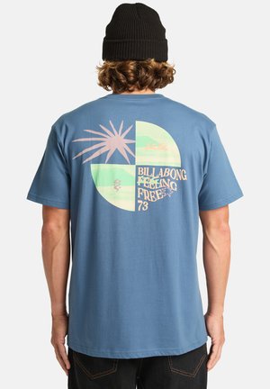 Modrá bavlněná tričko s kulatým grafickým designem na zádech, obsahující růžové slunce, zelené tvary a text "BILLABONG FEELING FREE 73."