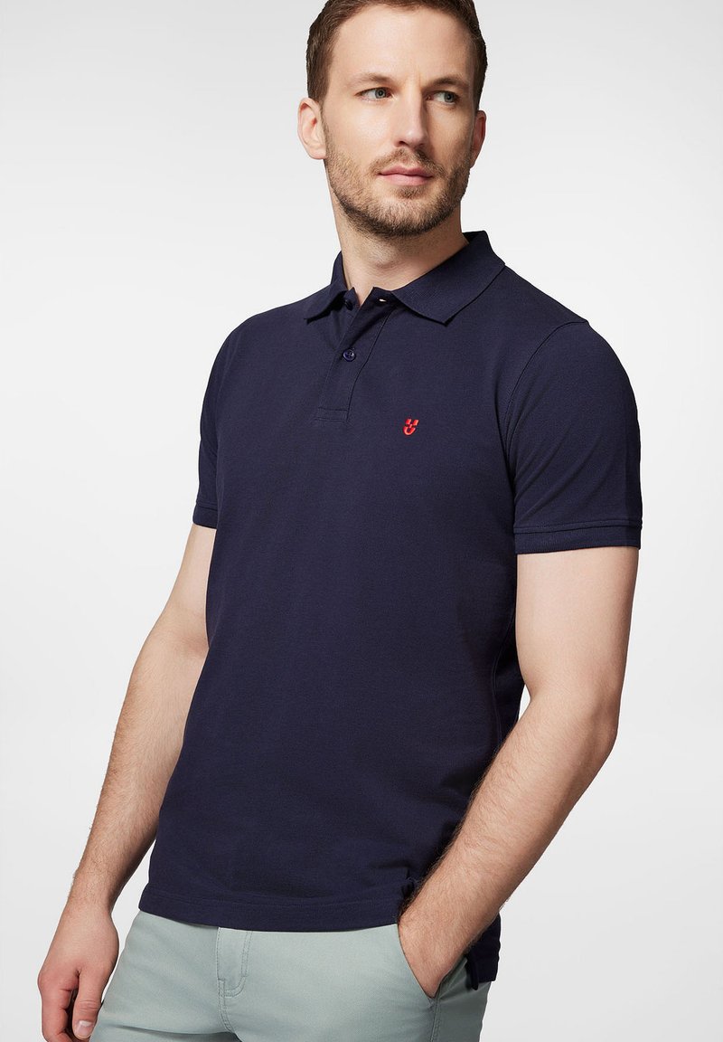 Granatowa koszulka polo z bawełny z trzema guzikami, krótkimi rękawami i małym czerwonym logo na piersi.