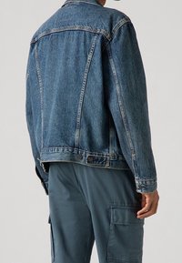 Jeansjacka i mellanblått med en klassisk modell, med sydda sömmar, knappade manschetter och en lätt sliten yta.