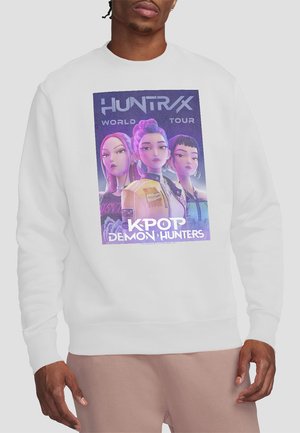 White sweatshirt featuring a graphic of three animated female K-pop characters with colorful hair and clothes, text "HUNTRX World Tour K-Pop Demon Hunters."