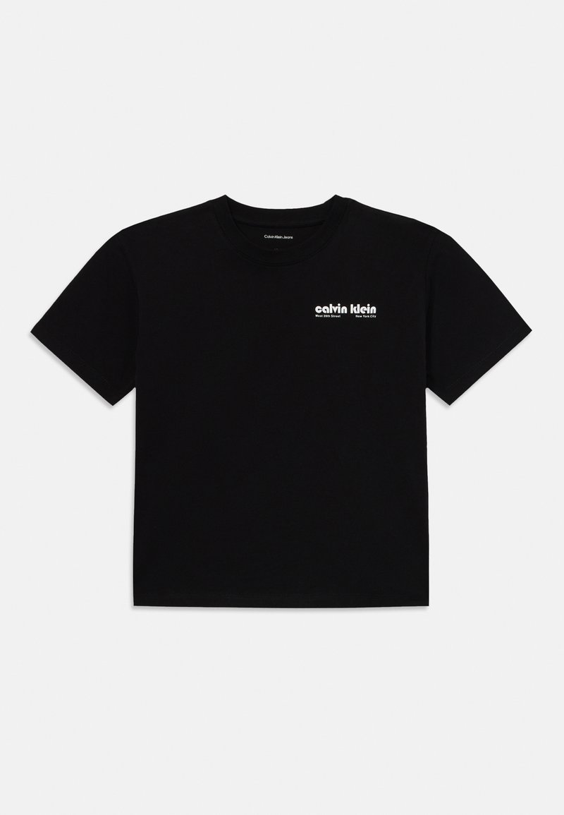 Melna kokvilnas T-kreklā ar apaļu kakla izgriezumu. Uz augšējā kreisā krūšu stūra ir balts logo teksts. Īsas piedurknes un brīva piegriezuma.