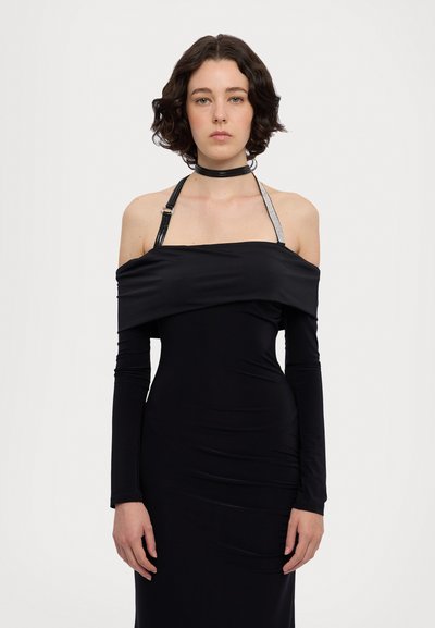 Robe noire décolletée avec des manches longues, silhouette ajustée et bretelles décoratives avec un accent métallisé. Tissu doux et extensible.