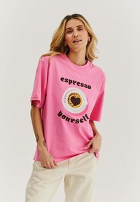 Růžové oversized tričko s krátkým rukávem s potiskem šálku kávy a textem "espresso yourself" v černé barvě. Měkký, pohodlný bavlněný materiál.