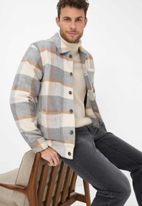 Veste-chemise à carreaux en crème, gris et rouille ; design à boutons ; texture douce ; avec une poche poitrine et deux poches latérales.