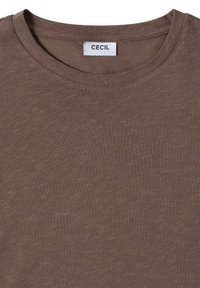 T-shirt marron à col rond avec une étiquette blanche affichant le nom de la marque "CECIL" cousue à l'intérieur du col.