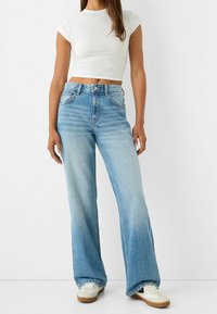 Ljusblå, vida jeans i denim med hög midja, fem fickor och subtil blekning. Kombineras med en vit figurnära topp.