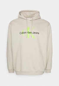 Hoodie beige con coulisse, caratterizzato da un grande logo "CK" nero e verde neon e dal testo "Calvin Klein Jeans" sul davanti. Materiale in cotone.