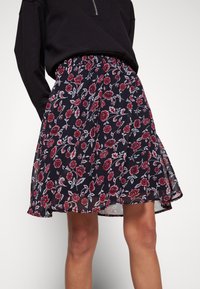 Blommig skaterkjol i genomskinlig marinblått tyg med ett röd- och vitblommigt mönster, med en elastisk midja och flaring nederkant.