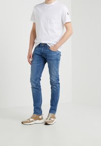 Herrvit t-shirt i bomull som matchas med blå slim-fit-jeans och beige sneakers. Outfiten har enkla, rena linjer utan synliga mönster.
