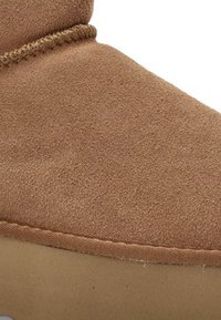 Botín de ante marrón con costuras visibles y suela de goma, mostrando un primer plano de la parte superior y el área del talón.