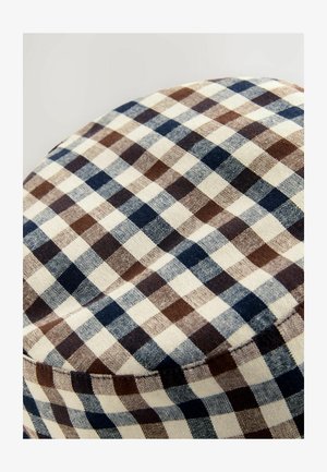 Barna, tengerészkék és krémszínű kockás anyag, amelynek varrott varrása kerek formát hoz létre, valószínűleg egy sapka vagy párna része.