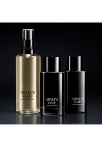 Tre Armani Code Eau de Parfum-flasker, en gjennomsiktig med spraypumpe, to svarte med lokk, vist mot en svart bakgrunn.