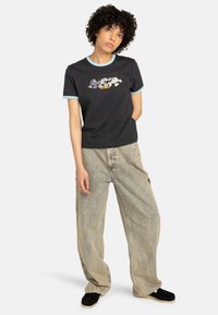 Czarna koszulka z jasno niebieskim wykończeniem, z kolorowym graficznym nadrukiem. Połączona z luźnymi, jasnymi dżinsowymi spodniami i czarnymi butami.