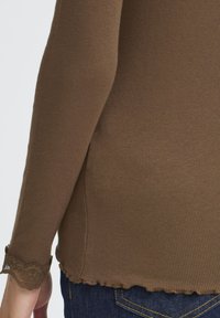 Brun ribbet langærmet top med scalloped lace kant ved håndled og nederste kant. Blødt stof, tætsiddende design, parret med mørke denim jeans.