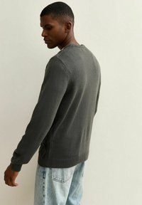 Suéter de punto verde oscuro con escote redondo, puños acanalados y detalles de punto en trenzado en los laterales. Llevado con jeans de lavado claro.