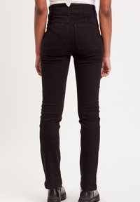 Jean noir taille haute avec un design ajusté, poches arrière et une légère texture. L'ourlet est droit et se termine au-dessus de la cheville.