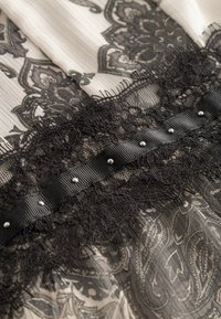 Schwarz-weißer Kleiderstoff mit filigranem Spitzenbesatz, einem Satinsband mit silbernen Nieten und einem Paisleymuster in der Basisschicht.