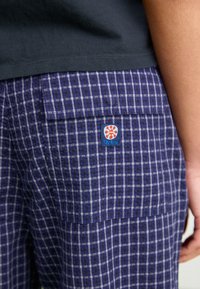 Plave karirane kratke hlače izrađene od lagane tkanine s prednjim džepom i oznakom logotipa. Imaju mrežasti uzorak u različitim nijansama.