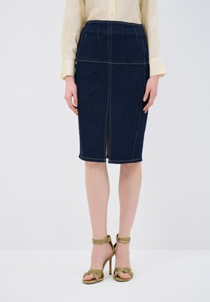 Donkerblauwe denim kokerrok met witte stiksels, knie-lengte, met een split aan de voorkant en een aansluitende pasvorm. Gestyled met groene sandaaltjes met banden.