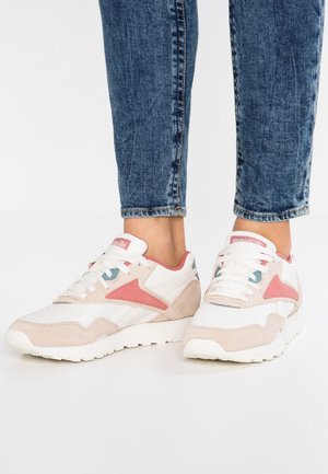 Hvide og lyserøde sportssko med læderdetaljer, der har en tekstureret sål, snørebånd og et logo på tungen. Bærer dem sammen med blå jeans.