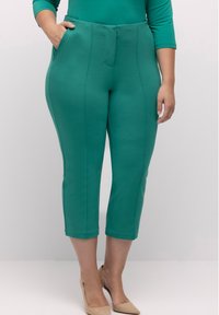 Vihreät capri-housut, jotka on valmistettu joustavasta kankaasta. Housuissa on sileä pinta, sivutaskut ja suora muotoilu hienovaraisella sauman yksityiskohdalla.