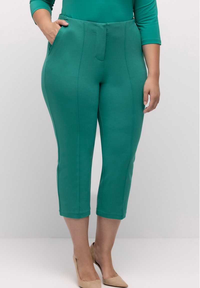 Vihreät capri-housut, jotka on valmistettu joustavasta kankaasta. Housuissa on sileä pinta, sivutaskut ja suora muotoilu hienovaraisella sauman yksityiskohdalla.