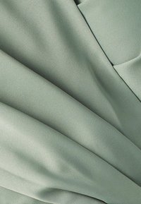 Svetlozelená látka s hladkou, matnou štruktúrou, ktorá má jemné záhyby a splývanie. Žiadne viditeľné vzory ani detaily hardware nie sú prítomné.