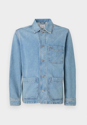 Veste en denim bleu clair avec un devant à boutons, un col pointu, deux poches avant et un petit logo crocodile vert sur la poche de poitrine.