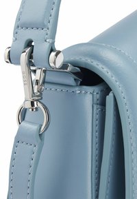 Lichtblauwe leren handtasdetail met een zilverkleurige metalen sluiting en gestikte schouderband. Heeft een gladde textuur en een gestructureerde vorm.