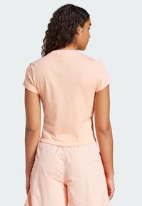 T-shirt à manches courtes de couleur pêche clair, fabriqué dans un tissu lisse avec une silhouette ajustée, associé à un pantalon rose ample.