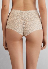 Beige lace trossor med blommönster, vågiga kanter och en mjuk textur som ger full täckning och en åtsittande design.