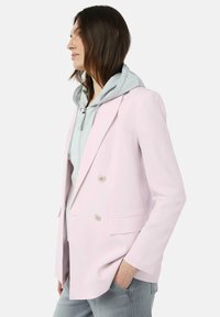Lichtroze dubbelzijdige blazer met parelknopen, zachte textuur, reverskraag en zijzakken, gelaagd over een lichtgrijze hoodie.