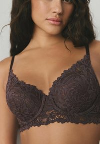 Lilla blonder-bh med en bølget kant, bløde skåle, justerbare stropper og indviklede blomsterdesigndetaljer over det hele.
