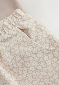 Lichtroze stof met een bloemenpatroon in een crèmekleur. Materiaal is zacht met een elastische tailleband. Het ontwerp bevat geplooide details nabij de tailleband.