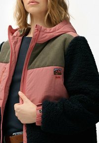 Fleece-voering jack met roze, olijfgroene en zwarte panelen, ribbelstructuur, ritsluiting en een subtiele logo patch op de borst.