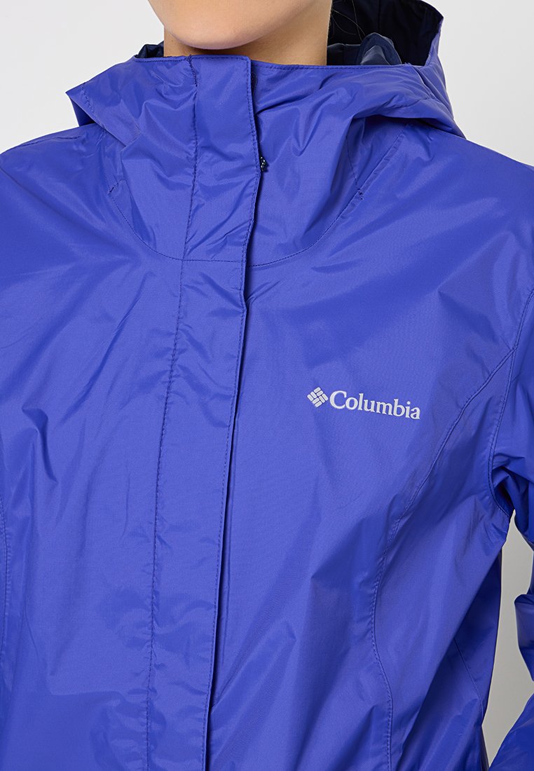 Veste imperméable violette avec un col haut, fermeture éclair à l'avant et logo sur la poitrine gauche. Tissu lisse et brillant avec un design ajusté.