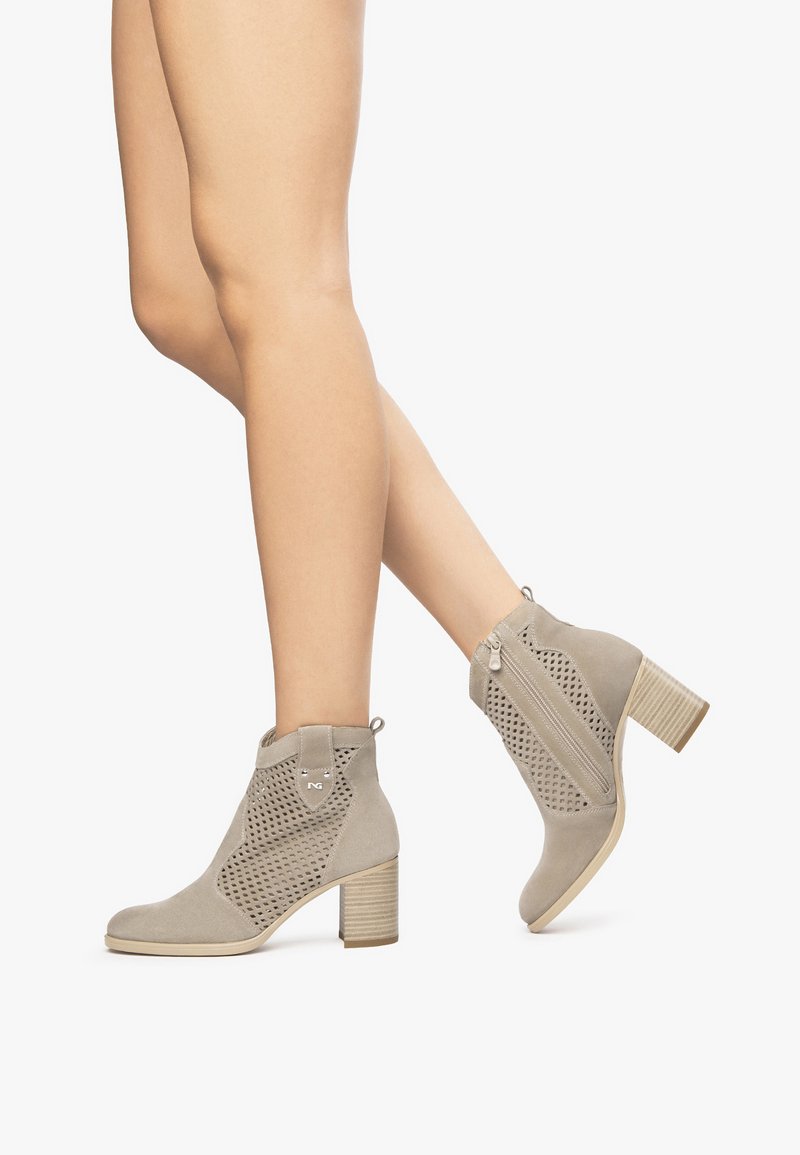 Botines de ante gris con lados perforados, tacón de bloque y cremallera lateral. Textura notable y elementos de diseño moderno.