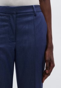 Námornícky modré nohavice na mieru z hladkej látky, s priamym strihom, pútkami na opasok a jemným leskom na povrchu.