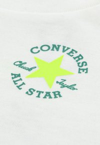 Λευκό ύφασμα με κεντρικό γραφικό που απεικονίζει πράσινο κείμενο "CONVERSE" και "ALL STAR", συνοδευόμενο από σχέδιο φωτεινού κίτρινου αστέρα.